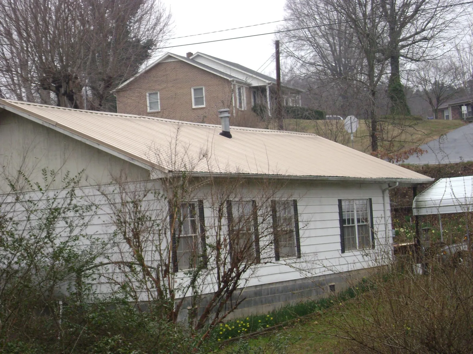 Tan metal roof on a white sided house set into a hillside — Commercial Roofing by Roofing Brothers in Charlotte